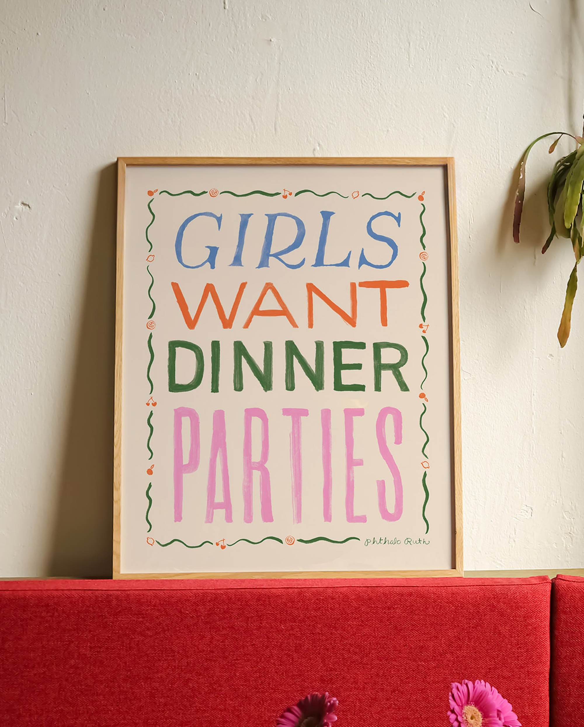 Framed art print featuring "Girls Want Dinner Parties" in colorful lettering, displayed in a red booth at a cafe.